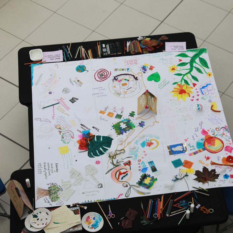 The finished community collage on a table, surrounded by pencils, paints and glue