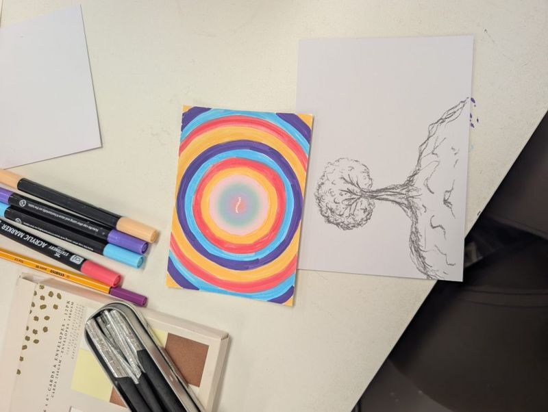 Postcards made at the workshop: a rainbow of rings and a pencil tree, with markers on the table